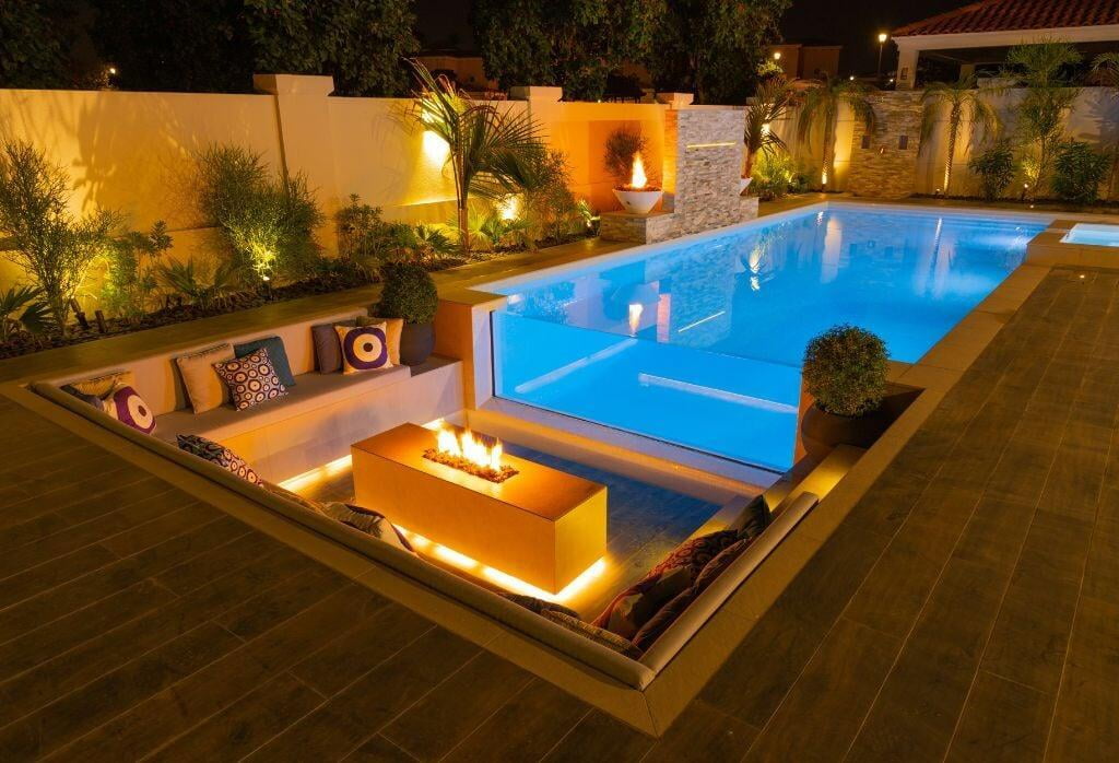 Infinity edge pool is surrounded by sunken seating, a fire pit, and planters.